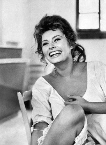 Actress Sophia Loren laughing while exchanging jokes during lunch break on a movie set.